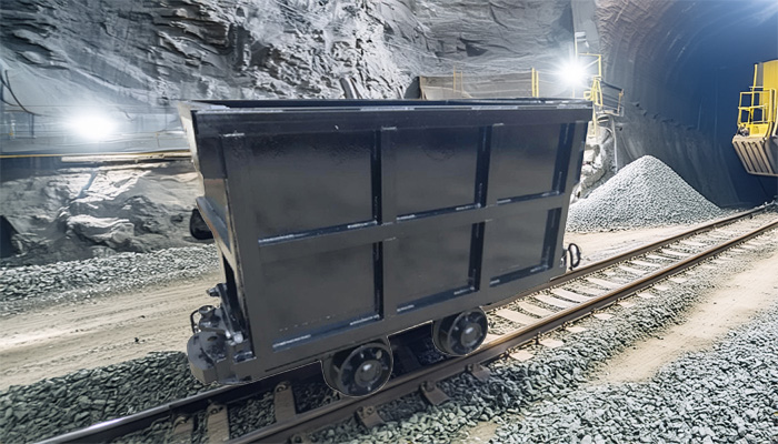 three distinct small industrial mining wagons (a flip-over type, a side-dump type, and a curved-rail side-dump type) positioned side-by-side in a dimly lit underground mine tunnel. 