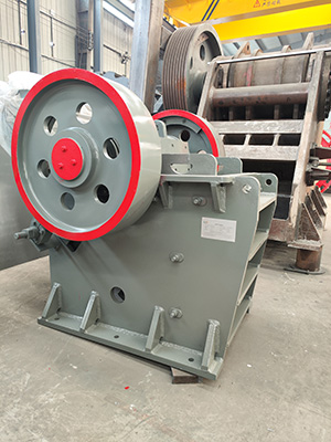 A white industrial jaw crusher positioned on the factory floor, undergoing final inspection before shipment.