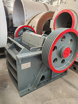 A white industrial jaw crusher positioned on the factory floor, undergoing final inspection before shipment.