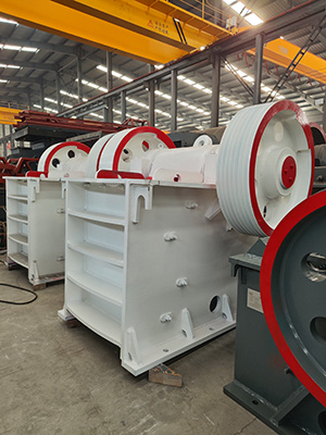 A white industrial jaw crusher positioned on the factory floor, undergoing final inspection before shipment.