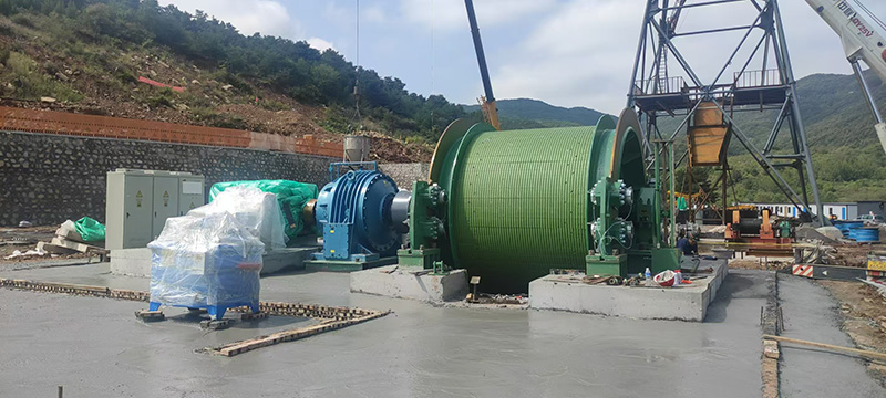 Mine hoisting system with industrial drum and headframe at sunset underground mining site.