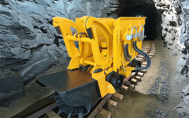 Pneumatic rock loader on rail tracks inside a narrow underground mine tunnel
